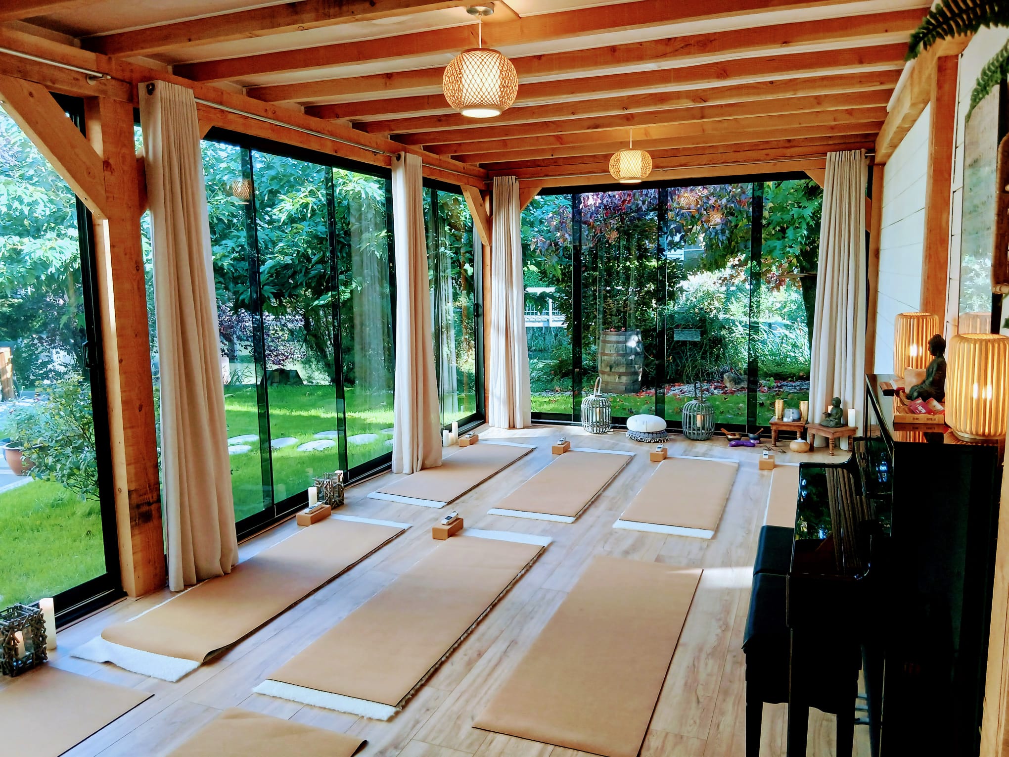 Studio van SensZenjoy met houten balken, grote glazen schuifpuien met uitzicht op de tuin en yogamatten op de vloer